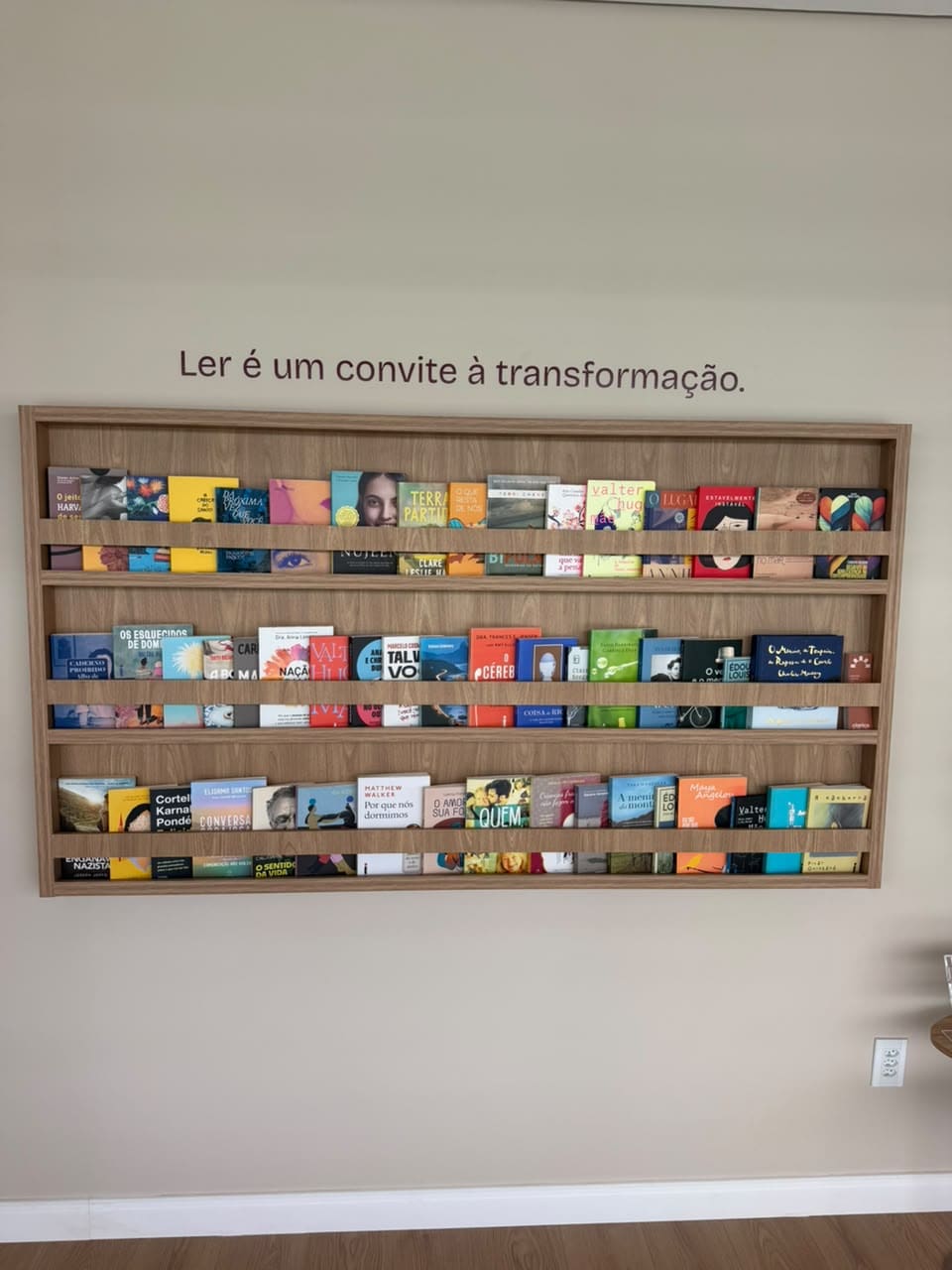 Parede de livros do consultório, com a frase Ler é um convite à transformação